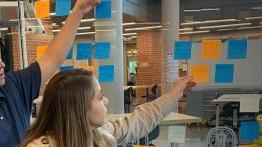 Students place sticky notes on a wall during an exercise in health innovation and entrepreneurship